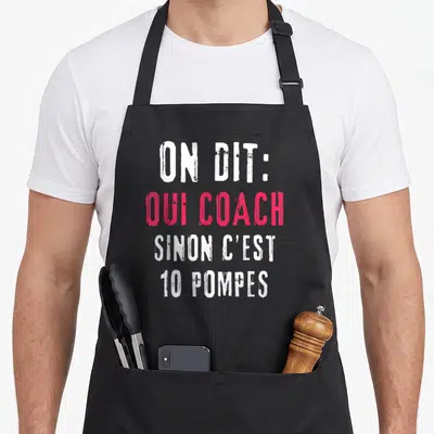 Tablier de cuisine noir avec l'inscription ON DIT OUI COACH SINON C'EST 10 POMPES en lettres blanches et roses.