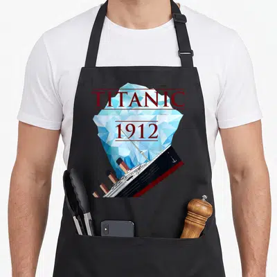 Tablier de cuisine noir avec illustration géométrique du Titanic 1912 et grand iceberg bleu en arrière-plan.