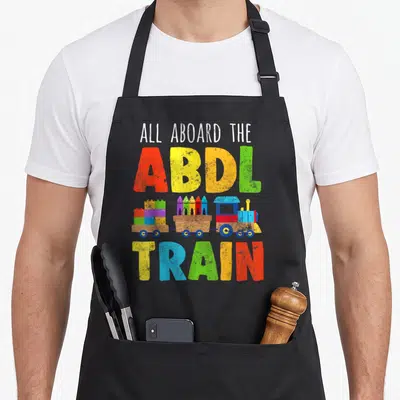 Tablier de cuisine noir avec un train en bois, des crayons et les mots ABDL Train en lettres multicolores.
