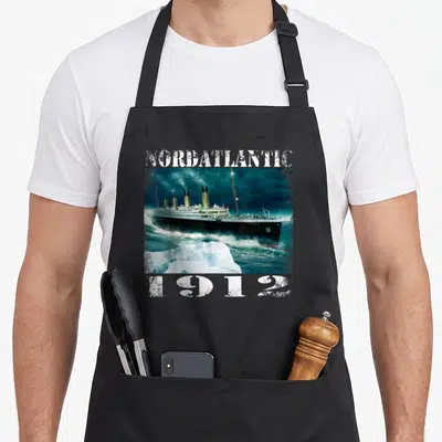 Tablier de cuisine noir avec illustration vintage d'un grand bateau noir naviguant près d'un iceberg sous un ciel bleu sombre et le texte Nordatlantique 1912.