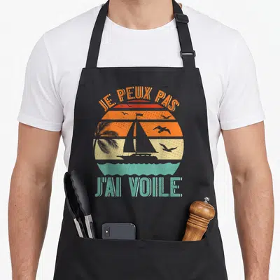 Tablier de cuisine noir avec un voilier, palmier et texte Je peux pas j'ai voile en style rétro.