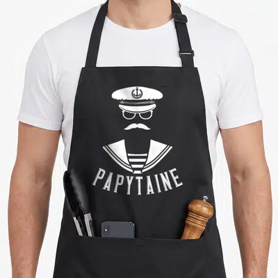 Tablier de cuisine noir avec illustration Capitaine Marin, moustache et inscription Papytaine en blanc.
