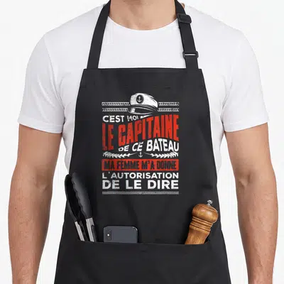 Tablier de cuisine noir avec illustration de casquette de capitaine et texte humoristique en rouge et blanc.