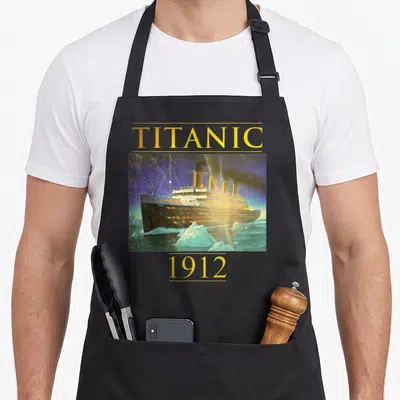 Tablier de cuisine noir avec illustration colorée du paquebot Titanic naviguant près d'icebergs sous un ciel étoilé.