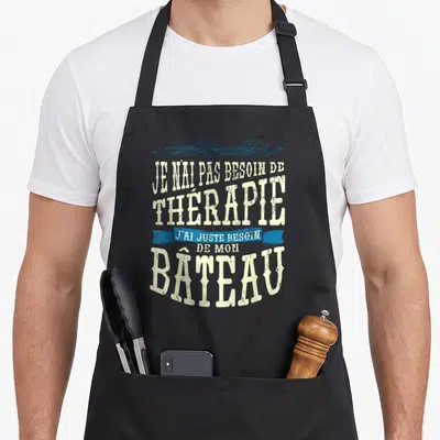 Tablier de cuisine noir avec inscription humoristique sur le thème du bateau et des vagues bleues en haut.