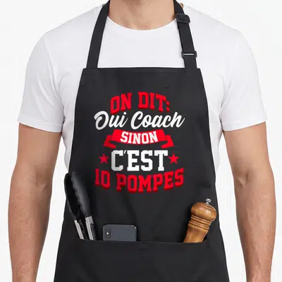 Tablier de cuisine noir avec le texte On Dit Oui Coach Sinon C'est 10 Pompes en rouge et blanc.