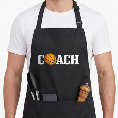 Tablier de cuisine noir avec le mot coach et une balle de basket orange stylisée en centre du design imprimé.