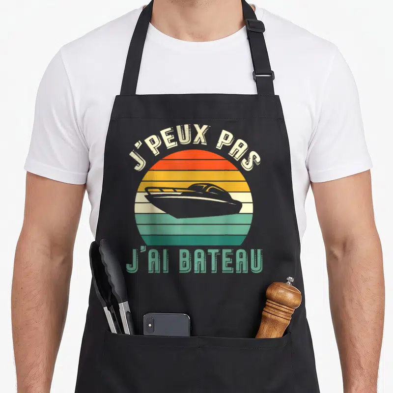 Tablier de cuisine noir avec illustration d'un bateau rapide sur fond de soleil couchant aux couleurs rétro.