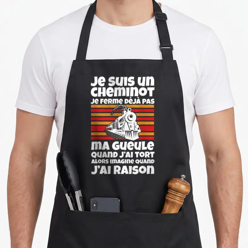 Tablier de cuisine noir avec une locomotive blanche et le texte Je suis un cheminot ma gueule sur bandes orange et rouges.