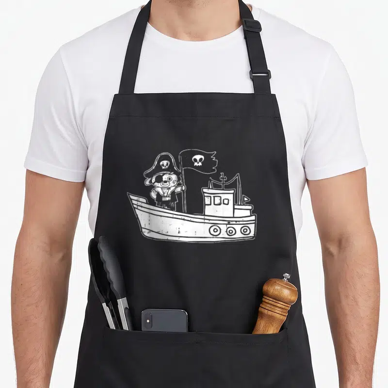 Tablier de cuisine noir avec illustration d'un bateau pirate naviguant sous un drapeau à tête de mort.