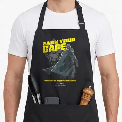 Tablier de cuisine noir avec une illustration d'un soldat en cape et le texte Earn Your Cape en jaune vif.