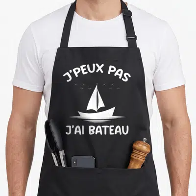 Tablier de cuisine noir avec inscription J'peux pas j'ai bateau et illustration de voilier blanc.