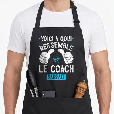 Tablier de cuisine noir avec deux pouces levés blancs, une étoile bleue et le texte voici à quoi ressemble le coach parfait en blanc et bleu.