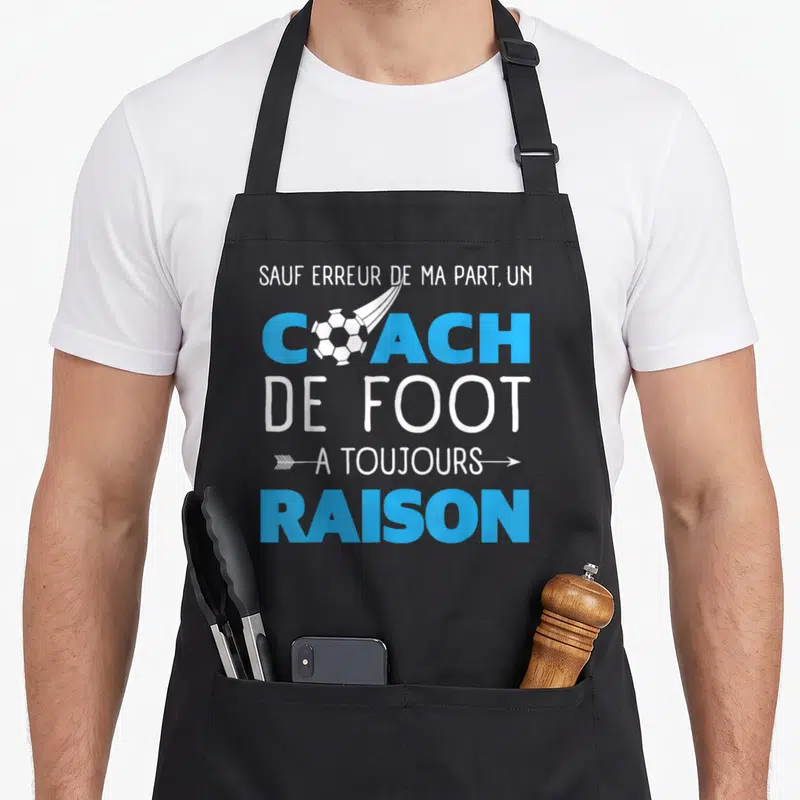 Tablier de cuisine noir avec inscription blanche et bleue sur le thème du coach de foot et d'un ballon stylisé.