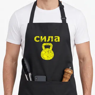 Tablier de cuisine noir avec illustration kettlebell jaune et texte forza en alphabet cyrillique.