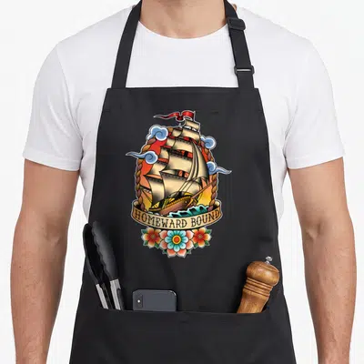 Tablier de cuisine noir avec illustration bateau à voile Homeward Bound style tatouage old school.