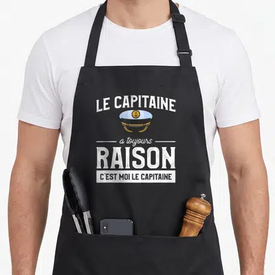 Tablier de cuisine noir avec une casquette de marin et le texte Le capitaine a toujours raison imprimé en blanc et gris.