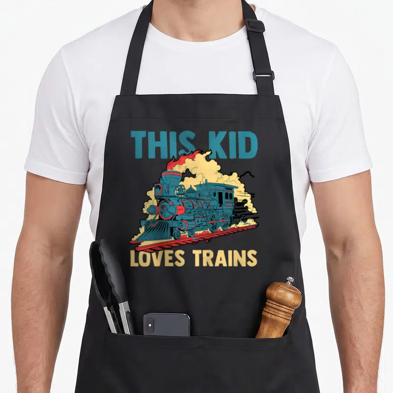 Tablier de cuisine noir avec illustration colorée d'une locomotive à vapeur sur rails et texte en anglais.