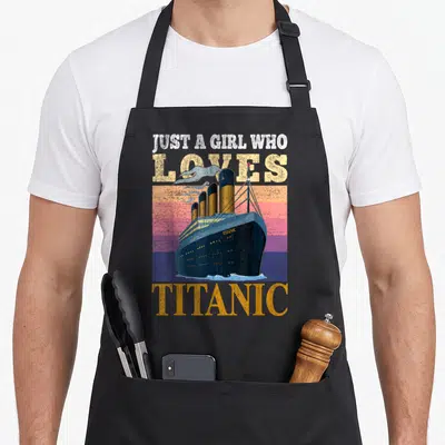 Tablier de cuisine noir avec illustration vintage d'un grand bateau et texte Juste une fille qui aime Titanic en lettres délavées.