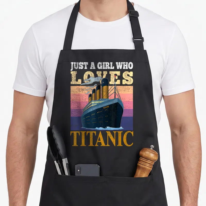 Tablier de cuisine noir avec illustration vintage d'un grand bateau et texte Juste une fille qui aime Titanic en lettres délavées.