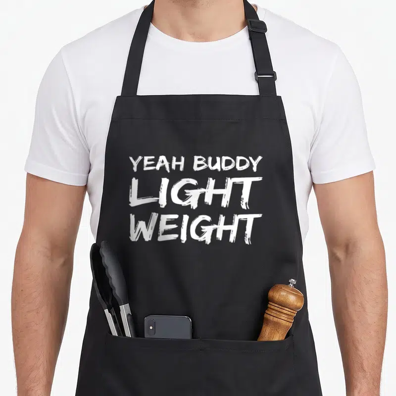 Tablier de cuisine noir avec l'inscription Yeah Buddy Light Weight en lettres blanches style brush.