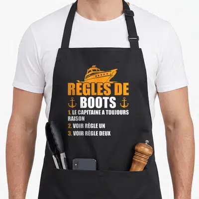 Tablier de cuisine noir avec illustration d'un yacht orange et texte Règles de Boots Le Capitaine A Toujours Raison.