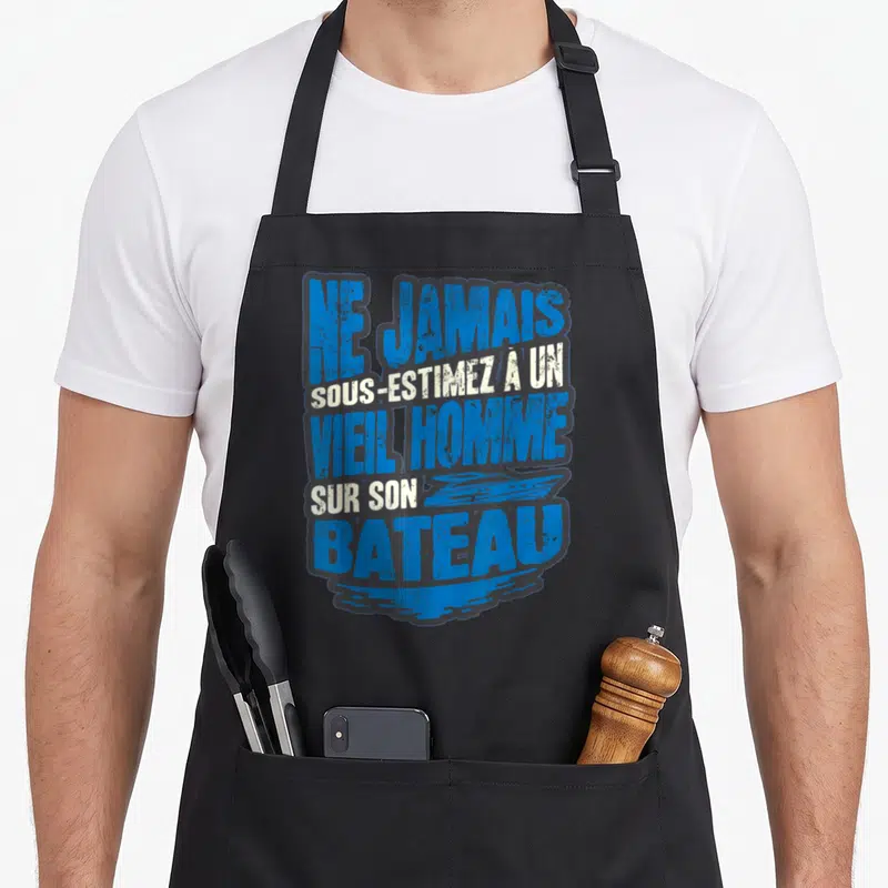 Tablier de cuisine noir avec inscription Ne jamais sous-estimez un vieil homme sur son bateau en bleu et blanc.