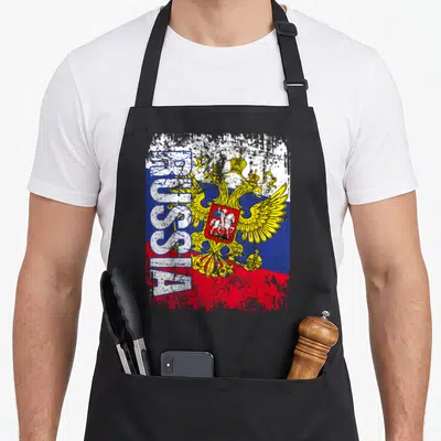 Tablier de cuisine noir avec le drapeau russe, le texte RUSSIA vertical et l'aigle bicephale doré sur fond texturé.