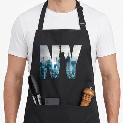 Tablier de cuisine noir avec un grand NY intégrant le paysage urbain de New York et la Statue de la Liberté en gris bleuté.