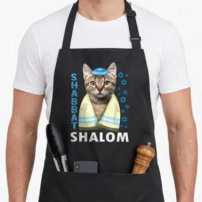 Tablier de cuisine noir avec illustration d'un chat tabby coiffé d'une kippa et enveloppé dans un tallit jaune.