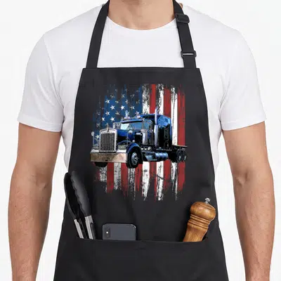 Tablier de cuisine noir avec illustration de trucker bleu et drapeau américain en arrière-plan texturé.