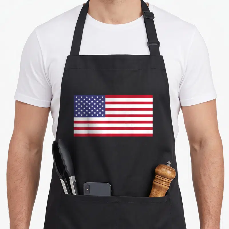 Tablier de cuisine noir représentant le drapeau des États-Unis avec ses étoiles et ses bandes rouges et blanches distinctives.
