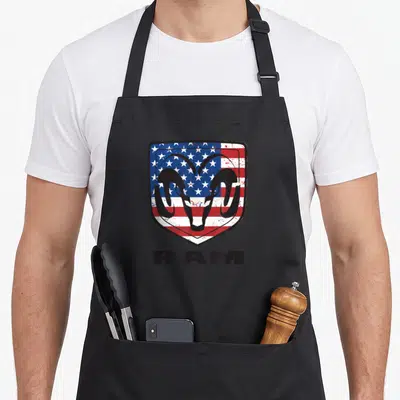 Tablier de cuisine noir avec le logo Ram Trucks Shield sur fond de drapeau américain et l'inscription RAM en bas.