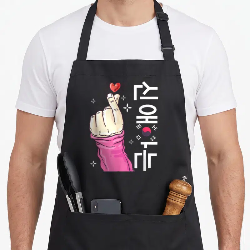 Tablier de cuisine noir avec main formant un doigt cœur, texte YOHAT et drapeau sud-coréen stylisé.