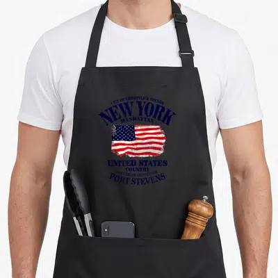 Tablier de cuisine noir avec un drapeau américain stylisé New York Manhattan et des inscriptions Port Stevens en bleu marine.