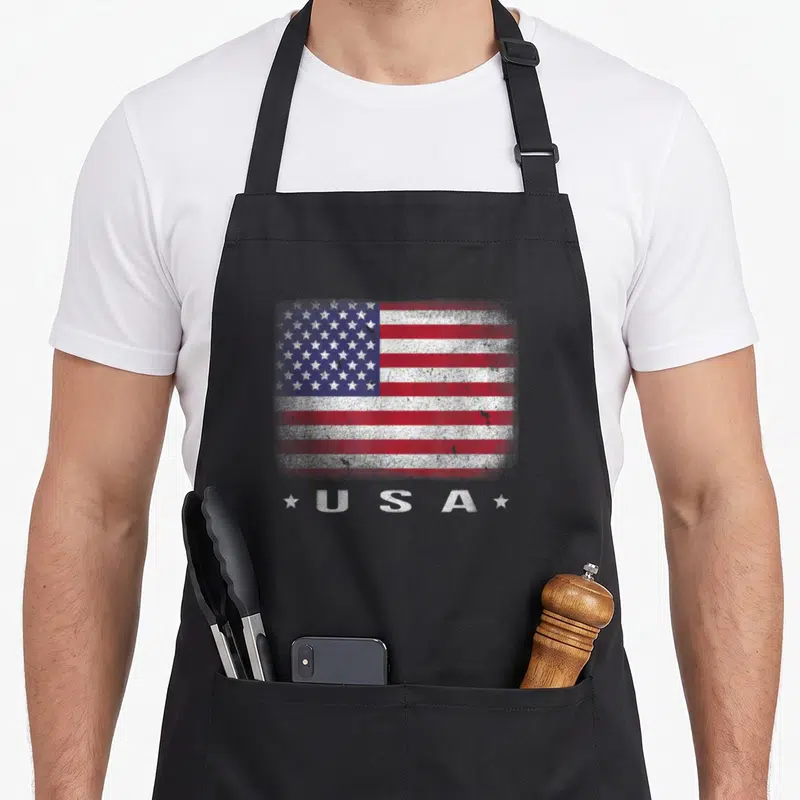 Tablier de cuisine noir avec drapeau américain délavé et inscription USA entre deux étoiles blanches.