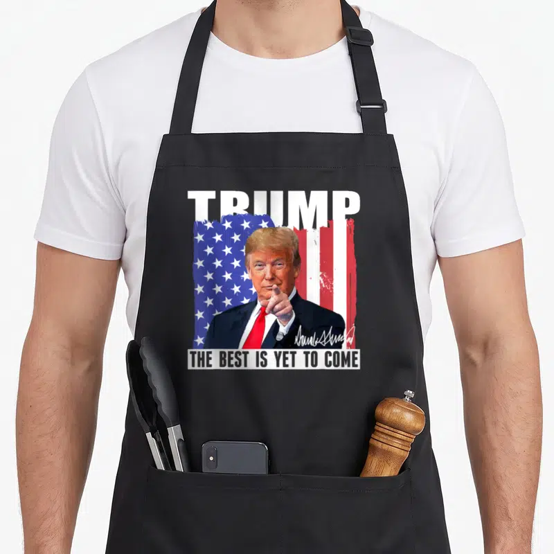 Tablier de cuisine noir avec portrait de Trump pointant devant un drapeau américain et le texte Trump The Best Is Yet To Come.