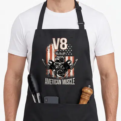 Tablier de cuisine noir avec illustration moteur V8 sur fond de drapeau américain dégradé et texte American Muscle en bas.