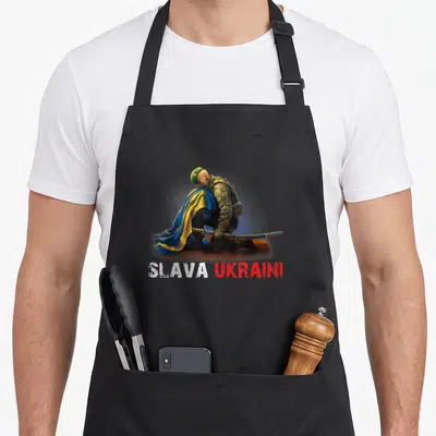 Tablier de cuisine noir avec un soldat agenouillé sous un drapeau bleu et jaune et le texte Slava Ukraini en blanc et rouge.