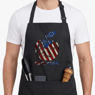 Tablier de cuisine noir avec une pomme aux couleurs du drapeau USA et les mots New York Brooklyn Queens imprimés en bas.