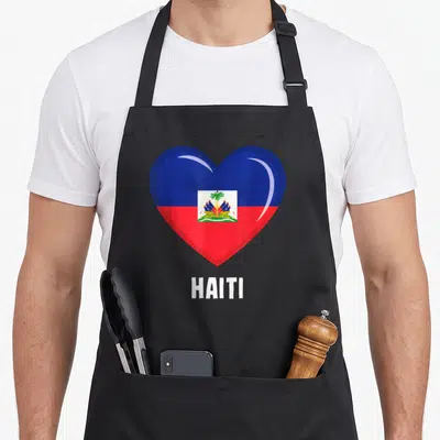 Tablier de cuisine noir avec un grand cœur aux couleurs du drapeau haïtien et l'inscription HAITI en dessous.