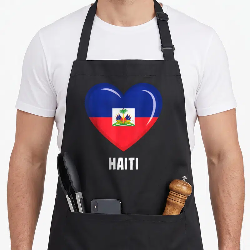 Tablier de cuisine noir avec un grand cœur aux couleurs du drapeau haïtien et l'inscription HAITI en dessous.
