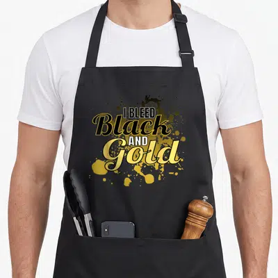 Tablier de cuisine noir avec inscription I Bleed Black and Gold en lettres dorées et noires sur fond d'éclaboussures.