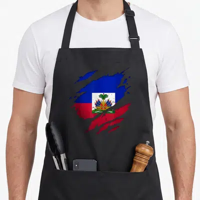 Tablier de cuisine noir avec drapeau Haïti stylisé en éclaboussure et emblème central coloré.