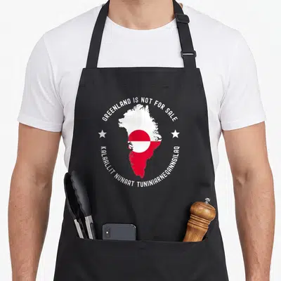 Tablier de cuisine noir avec la carte du Groenland, son drapeau et des étoiles blanches sur fond gris uni.