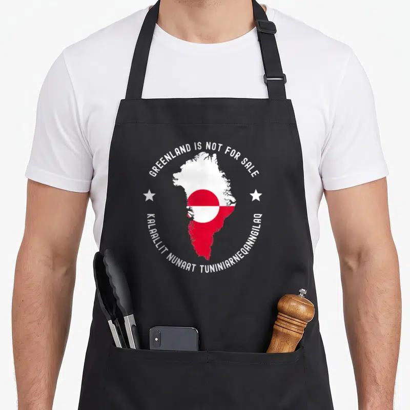 Tablier de cuisine noir avec la carte du Groenland, son drapeau et des étoiles blanches sur fond gris uni.