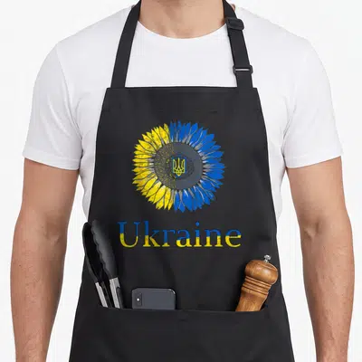 Tablier de cuisine noir avec un grand tournesol bicolore et le mot Ukraine imprimé en dessous.