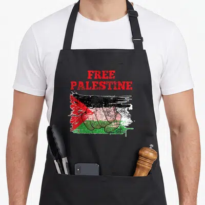 Tablier de cuisine noir avec un poing fermé coloré aux teintes du drapeau palestinien et du texte en rouge.