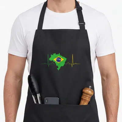 Tablier de cuisine noir avec carte du Brésil en forme de cœur et ligne d'ECG verte et jaune sur fond gris uni.