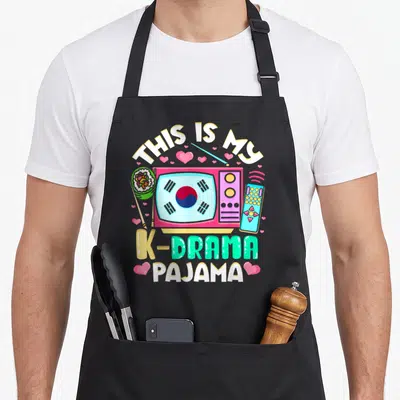 Tablier de cuisine noir avec illustration colorée représentant un téléviseur rose au drapeau sud-coréen, une télécommande et des cœurs roses.